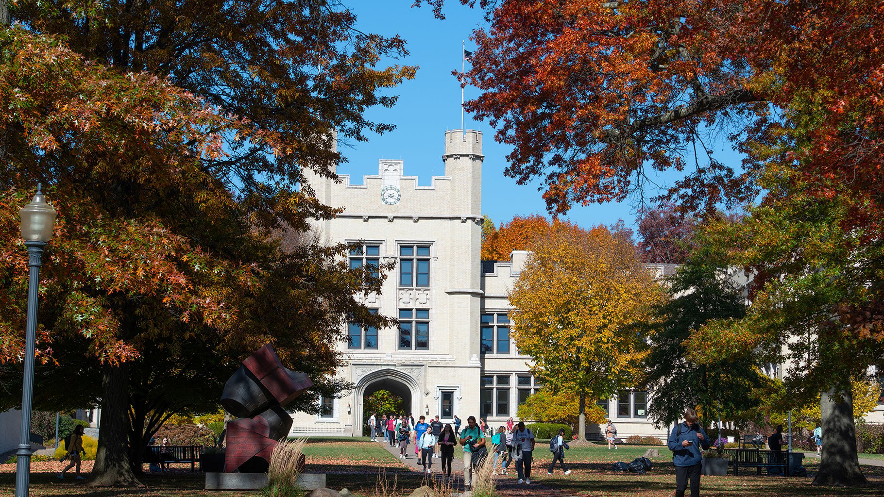 Students walk beneath colorful autumn trees in front of Kauke Hall at The College of Wooster.