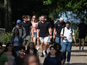 Students carrying backpacks walk along a tree-lined campus path at The College of Wooster.