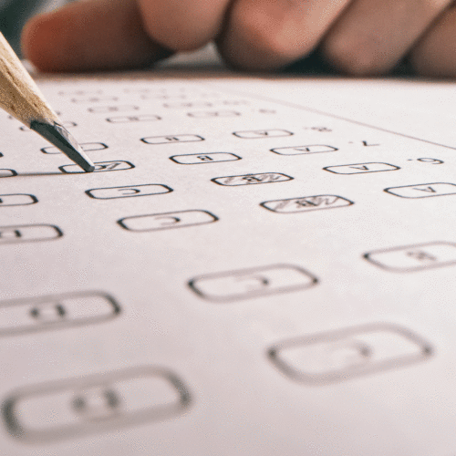 Close up of a standardized test form with a hand resting on the paper and a pencil