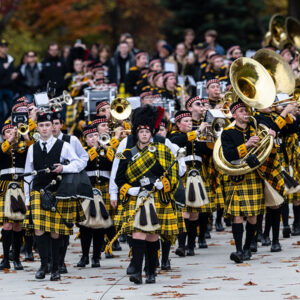 The College of Wooster marching band marches in uniform with alumni and families trailing behind.