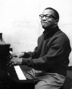 Jazz Musician Billy Strayhorn seated at a piano with hands on the keyboard