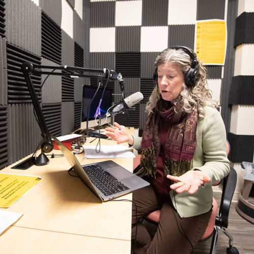 Denise Bostdorff, professor of communication studies at The College of Wooster, sits in front of a laptop in a sound studio with a microphone and headphones