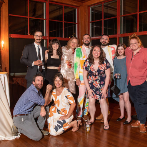 10 wedding members pose in 2 rows to commemorate Von Chorbajian and Michael DiPietro's marriage. The couple and 5 others smile in the back row. 2 people kneel with their hands clasped in the front row and one smiles with their hands on their knees.