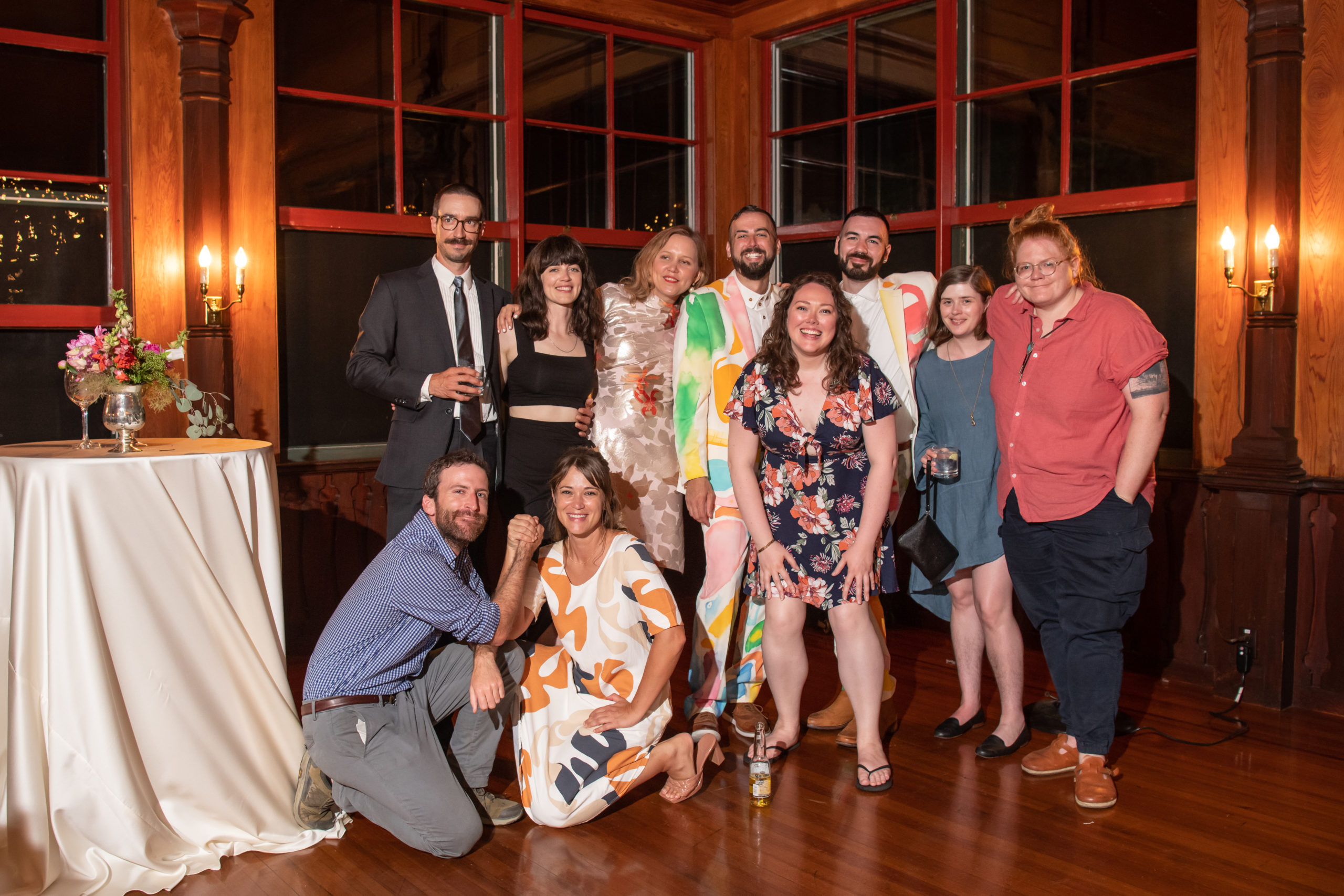 10 wedding members pose in 2 rows to commemorate Von Chorbajian and Michael DiPietro's marriage. The couple and 5 others smile in the back row. 2 people kneel with their hands clasped in the front row and one smiles with their hands on their knees.