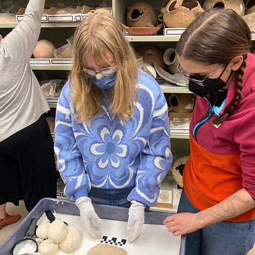 Students, Emily Voneman '25 and Maura Ellenberger '25 review items in the collection from Pella.