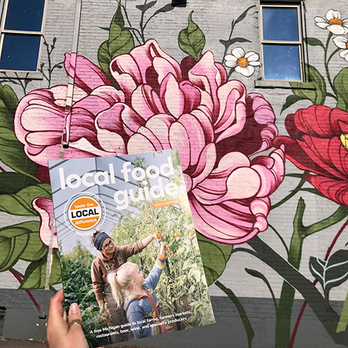 Local Food Guide magazine held in front of mural of flowers