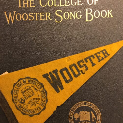 Photograph of the cover of "The College of Wooster Song Book" featuring and embossed seal of the college and a Wooster pennant.
