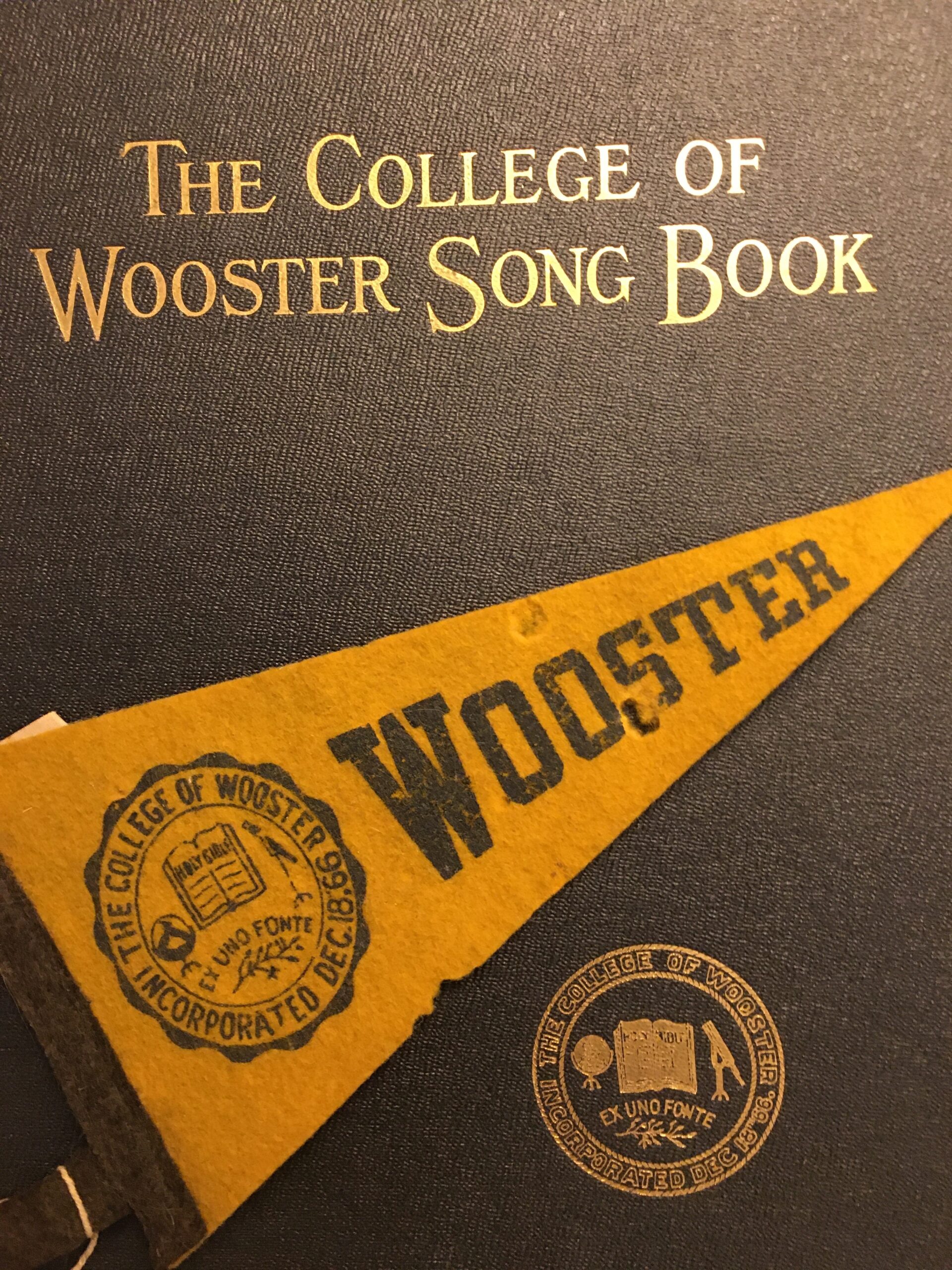 Photograph of the cover of "The College of Wooster Song Book" featuring and embossed seal of the college and a Wooster pennant.