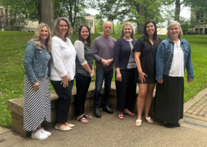 Staff members of the Academic Resource Center at The College of Wooster pose outdoors in a row, smiling, with trees and campus buildings in the background.