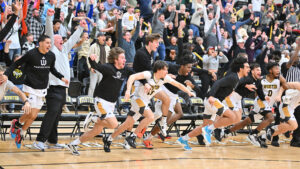 Wooster men’s basketball players and fans erupt in celebration, jumping off the bench with arms raised after a thrilling play at Timken Gymnasium.