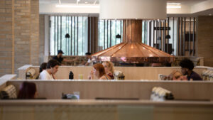 Students sitting in booths and dining at the Lowry Center at The College of Wooster, with a copper hood fixture in the background.