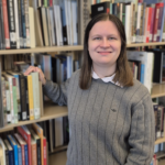 A headshot of Sarah Wallenfelsz standing in front of the library shelves